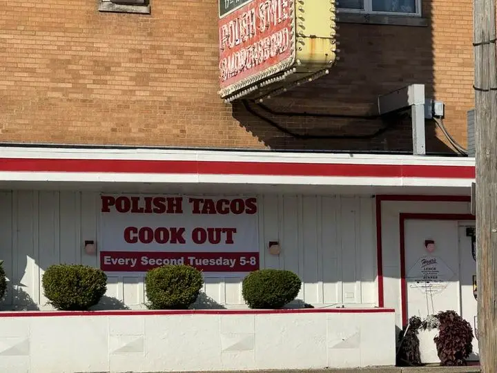 A photo of a brick building with a sign that reads 'POLISH TACOS COOK OUT Every Second Tuesday 5-8'. The building has a red…