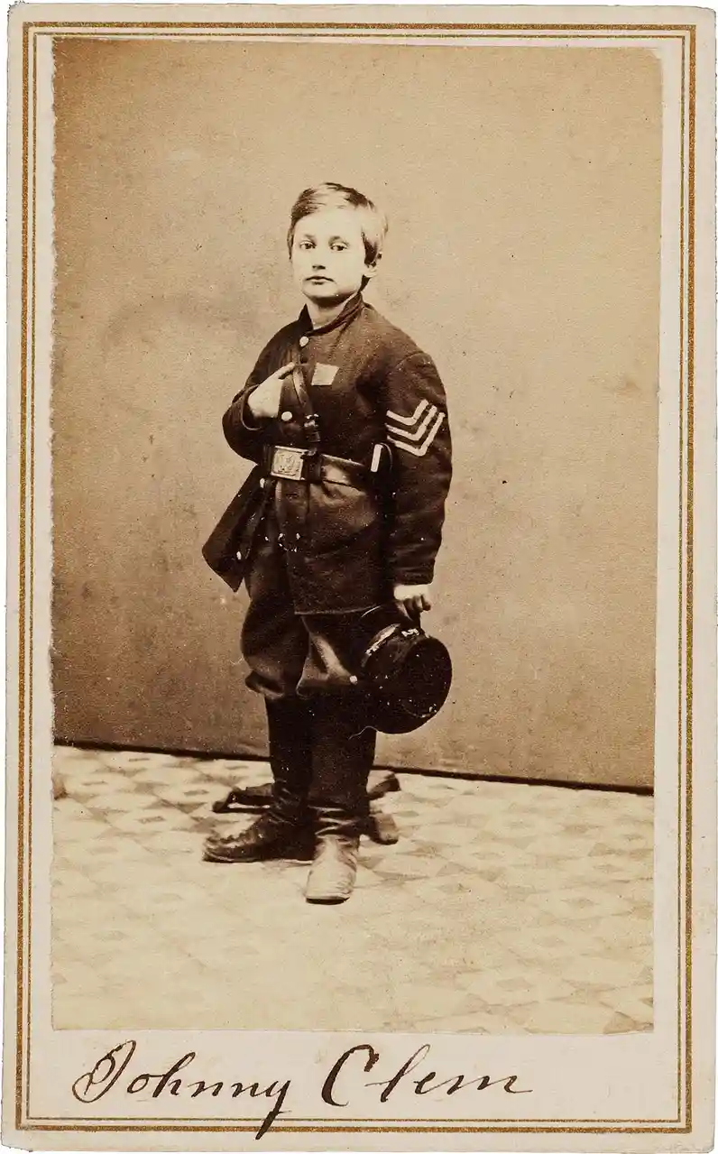 A sepia-toned vintage portrait of a young boy, identified by handwritten text at the bottom as 'Johnny Clem', dressed in a…