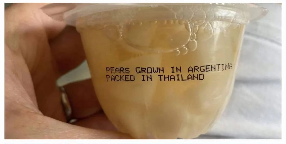 A hand holds a clear plastic cup filled with sliced fruit, likely pears, showing printed text that reads 'PEARS GROWN IN…