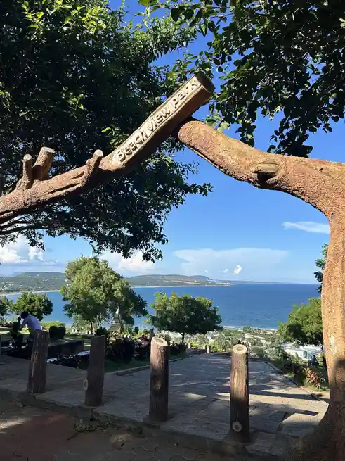 A scenic photo of a wooden archway entrance to 'Beach View Park' with carved lettering, framing a view of a blue ocean…