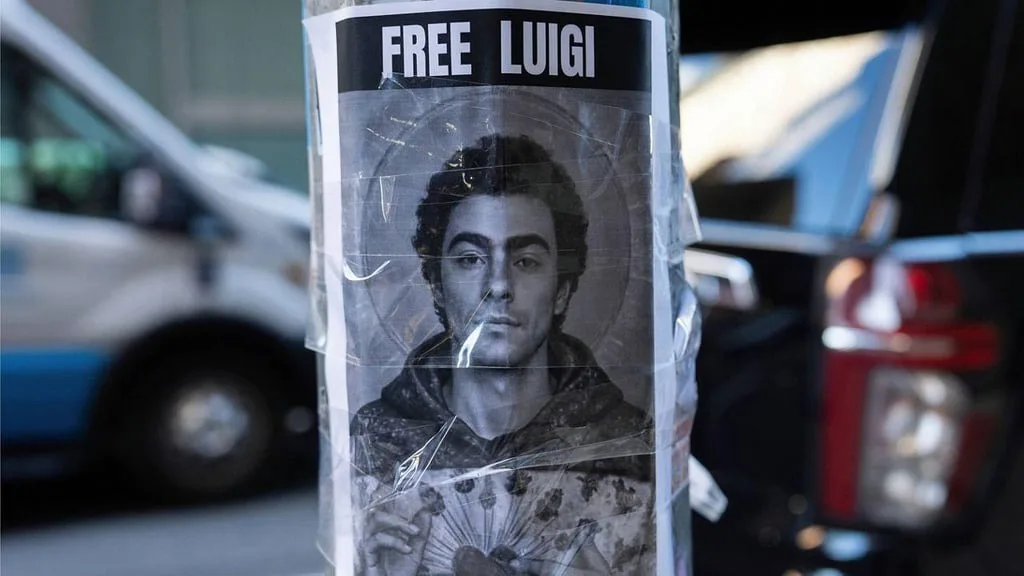 A black-and-white poster of a man with a halo, resembling a saint, is taped to a pole outdoors with cars in the background…