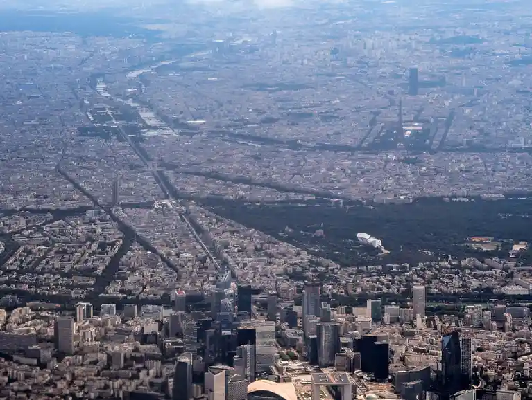 An aerial view of Paris, France, showing the cityscape with the Eiffel Tower visible in the distance, surrounded by dense…