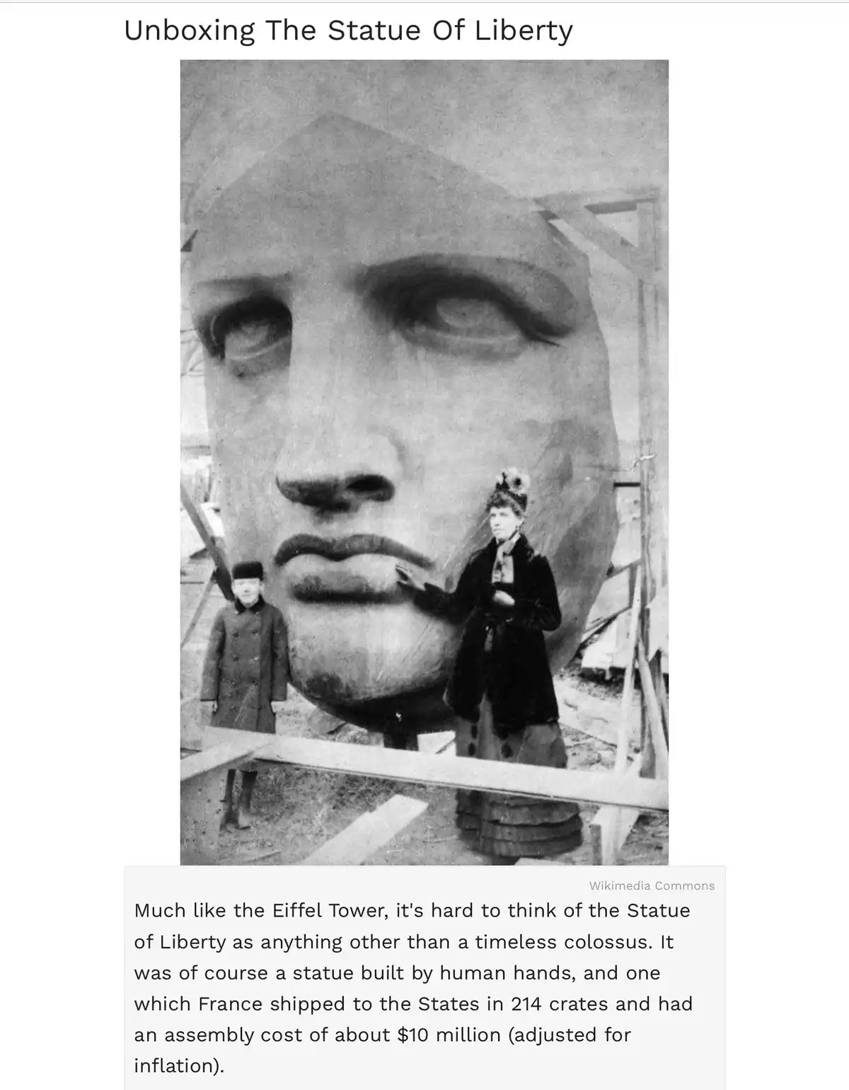 A historical black-and-white photo shows the head of the Statue of Liberty during assembly, with two people standing in…