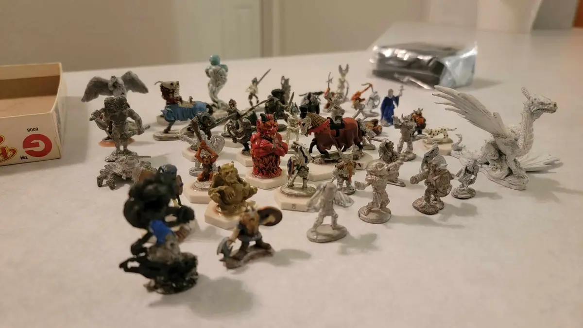 A collection of painted and unpainted fantasy miniatures, including a large white dragon, a red demon, and various warriors…