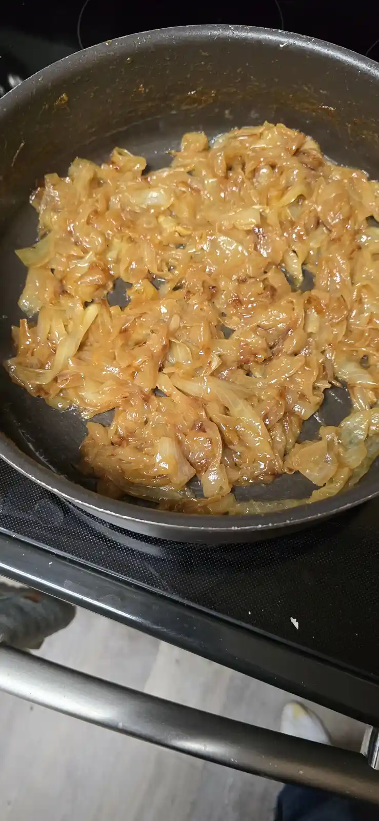 A close-up photo shows a dark frying pan on a stovetop filled with golden-brown, glossy caramelized onions. The onions are…