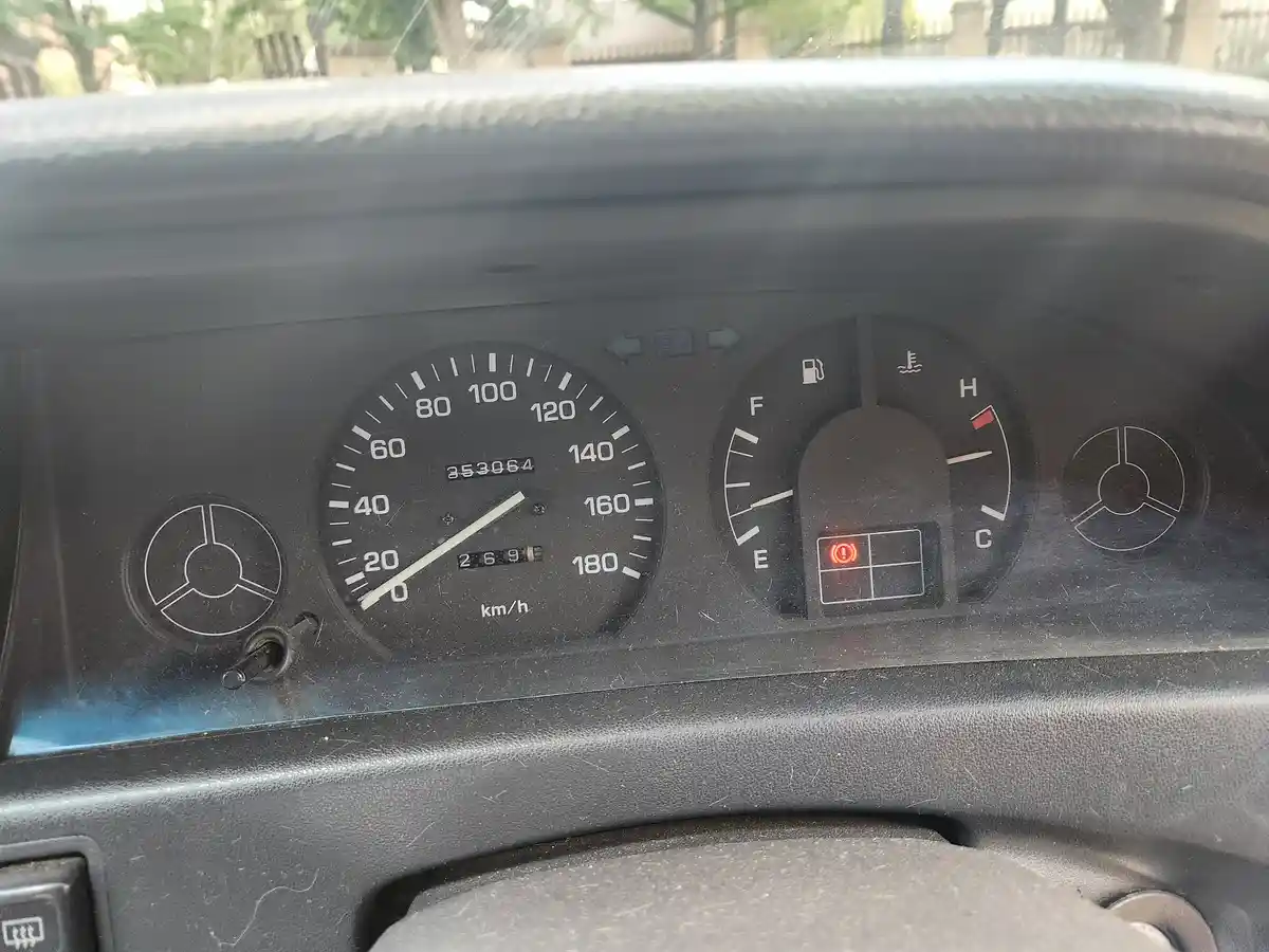 A close-up of a car's dashboard showing a speedometer, fuel gauge, and temperature gauge, with the engine check light…