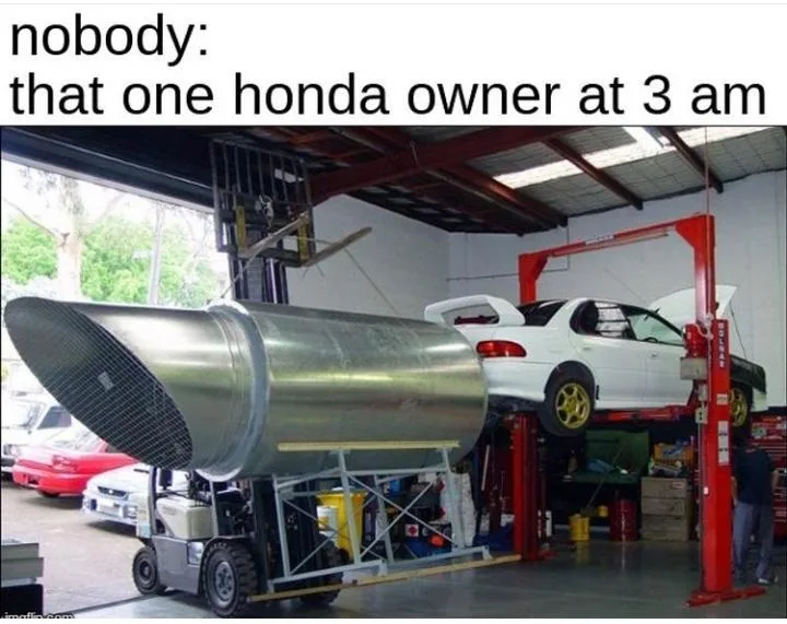 A white Honda car is elevated on a red car lift in a garage. A forklift is pushing a massive, industrial-sized metal exhaust…
