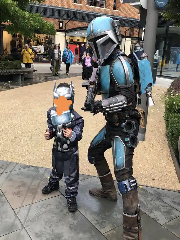 A child in a Thor costume with their face obscured by an orange blur stands next to a full-sized adult cosplayer dressed as…