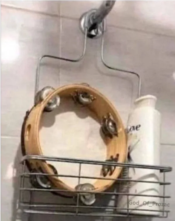 A wooden tambourine with metal jingles sits in a metal shower caddy next to a white bottle, with a showerhead above. The…