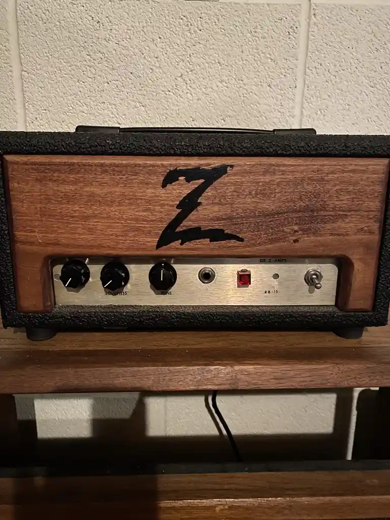 A close-up of a wooden guitar amplifier head with a large black 'Z' logo on the front panel. The control panel features…