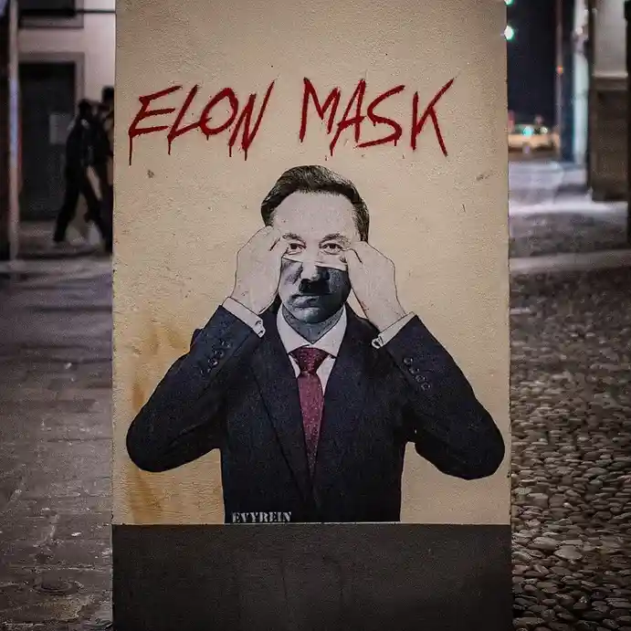 A street poster shows a man in a suit and tie pulling down a mask over his face, with the words 'ELON MASK' written in red…