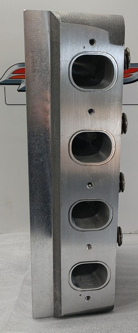 A vertical close-up of a metallic engine block with four oval-shaped cylinder bores visible in a row. The block has a…