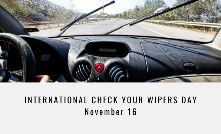 A photo taken from inside a car shows a dashboard and windshield with wipers raised, looking out onto a sunny highway. The…