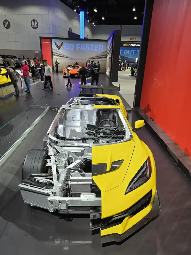A yellow Chevrolet Corvette on display at an auto show is cut in half, revealing its exposed silver metal chassis and…