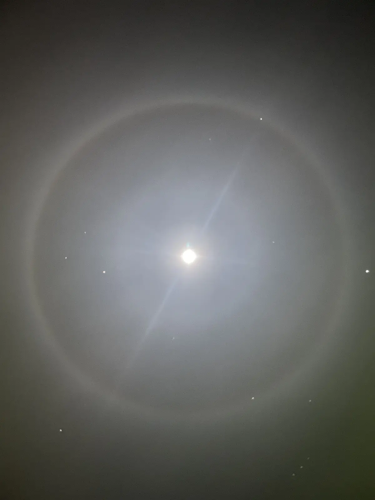 A photograph of the sun with a faint, circular halo visible around it, set against a hazy, gray sky with a few distant…
