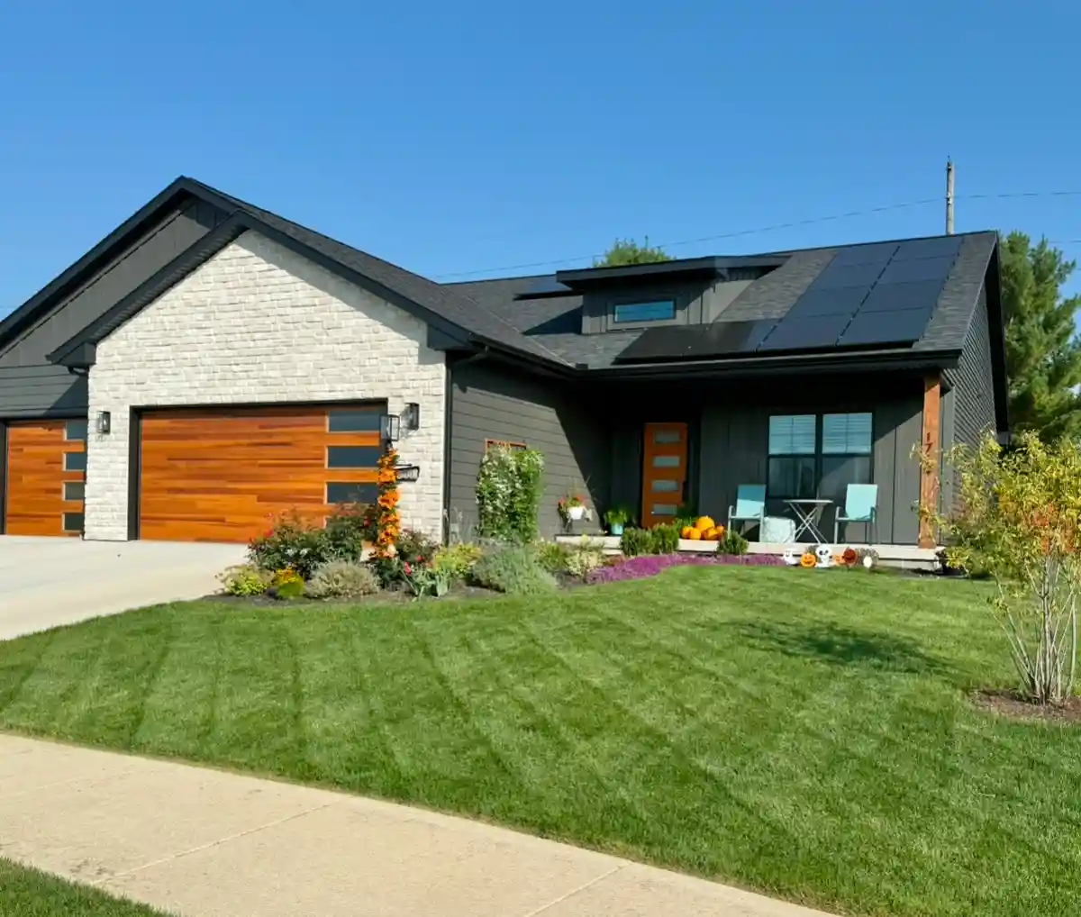 a modern house with a neatly mowed lawn, solar panels on the roof, and a clean front yard with pumpkins and decorations. the…