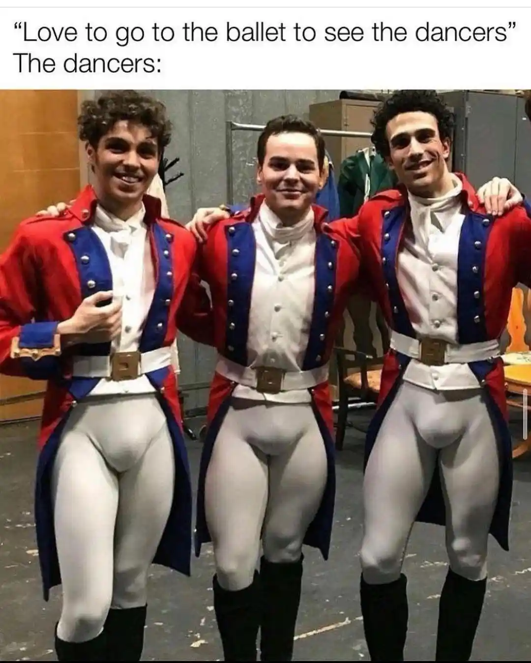 Three male ballet dancers in red and blue military-style costumes with white tights and black boots pose together backstage…