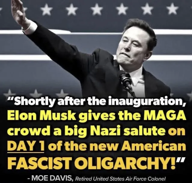 A black and white photo of Elon Musk raising his right arm in a salute, standing before a backdrop with stars and stripes…