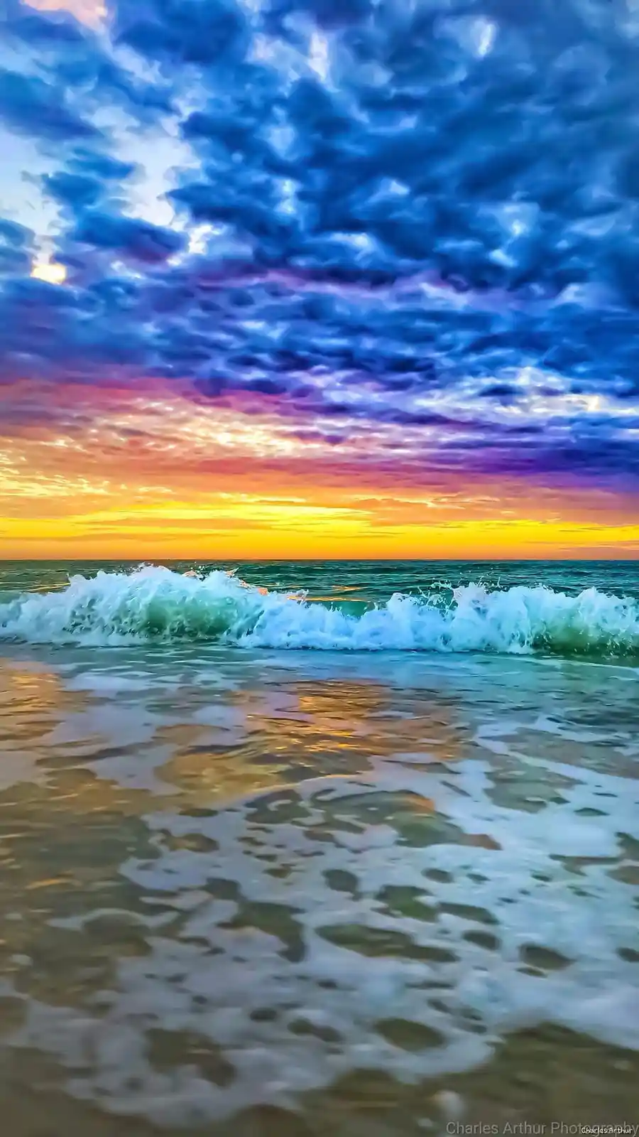 A vibrant, colorful beach sunset photo showing crashing ocean waves in the foreground, with a sky filled with dramatic blue…