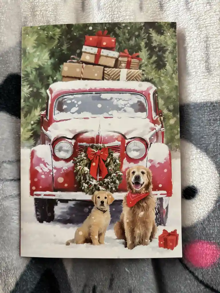A Christmas card image shows a red vintage truck covered in snow, decorated with a wreath and piled high with wrapped…