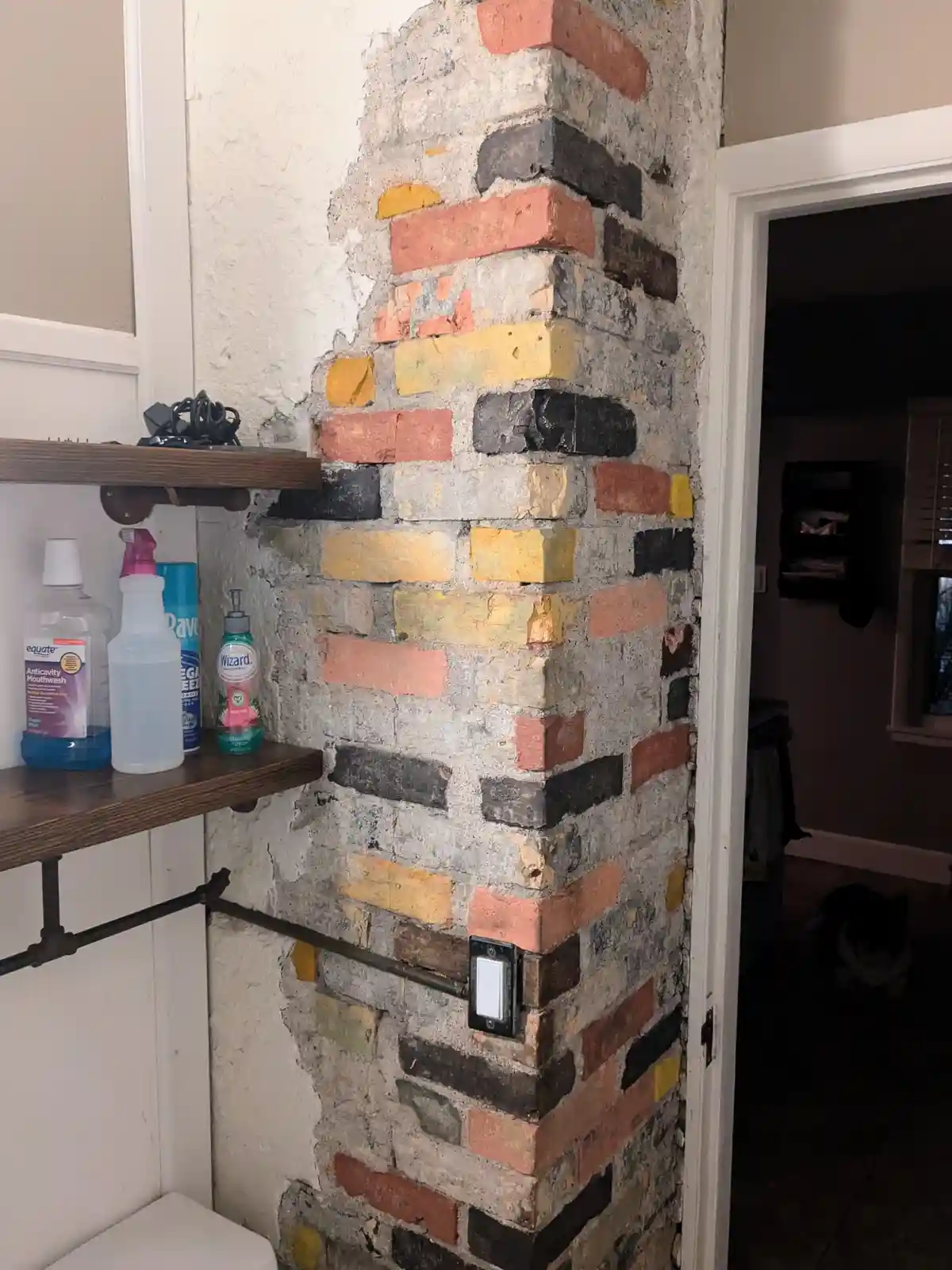 A bathroom corner shows a wall with a section of brickwork painted in various colors including red, yellow, black, and gray…
