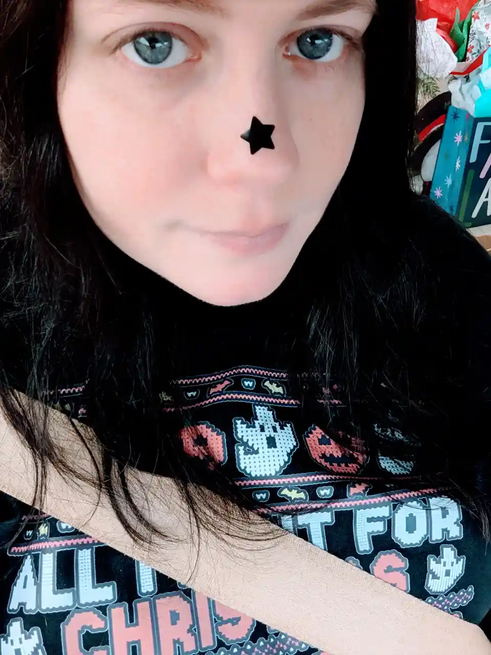 A person with dark hair and blue eyes looks directly at the camera, wearing a black turtleneck sweater with pixel art…
