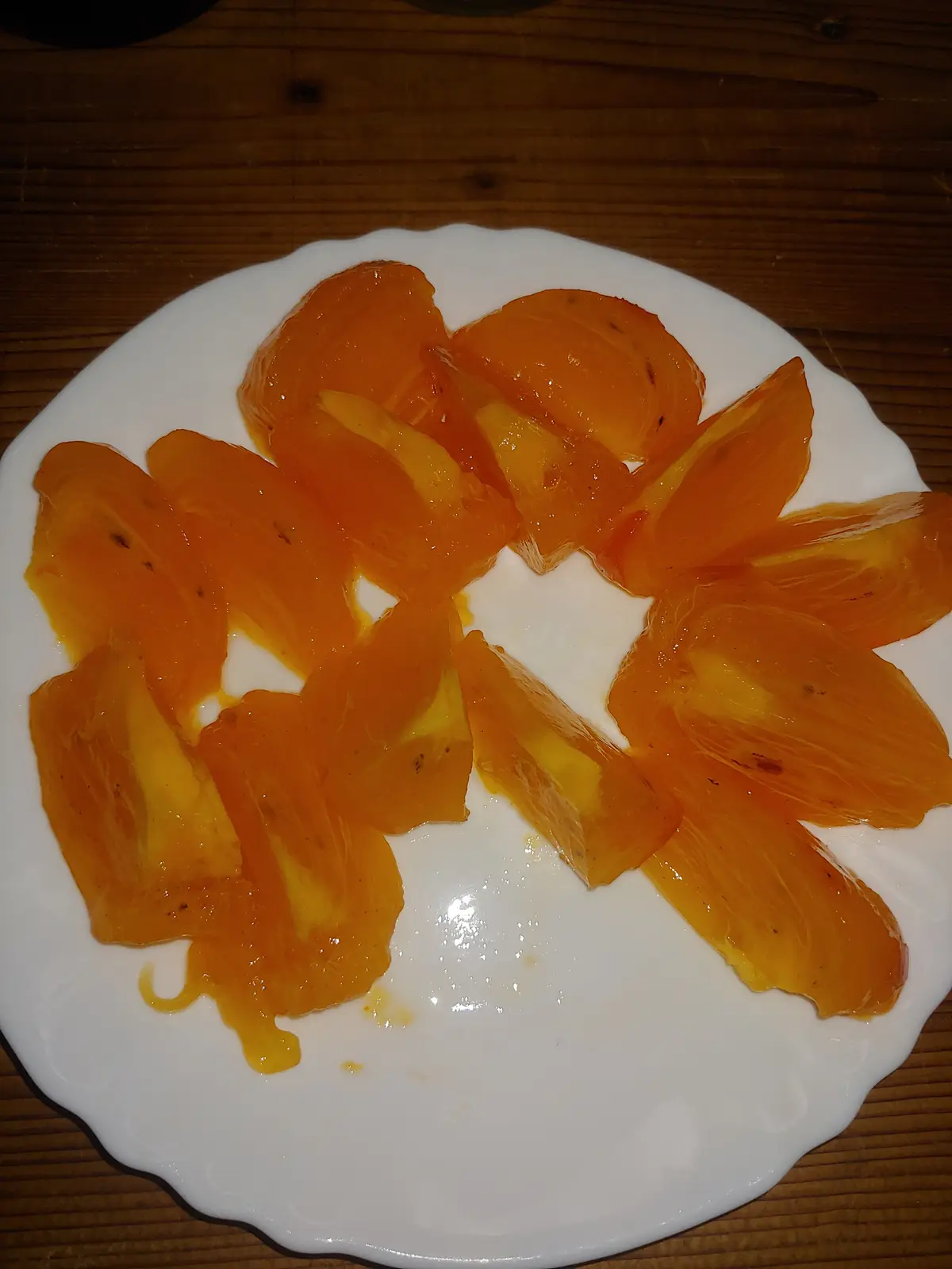 A white plate with orange-colored, translucent, gelatinous-looking food arranged in a circular pattern on a wooden table…
