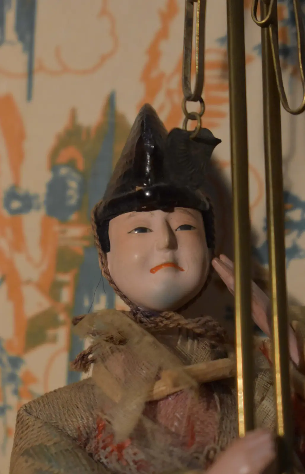 A close-up of a traditional Japanese doll with a painted face, wearing a black hat and textured fabric clothing, hanging…