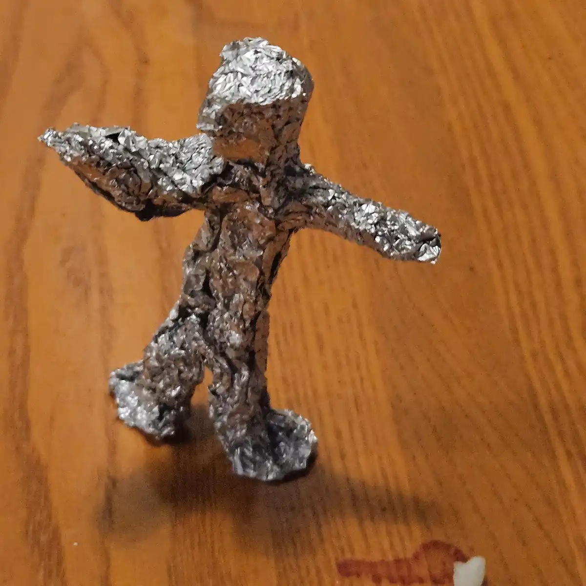 A crumpled foil figure with arms and legs spread out stands on a wooden surface. The text overlaid on the image reads 'i…