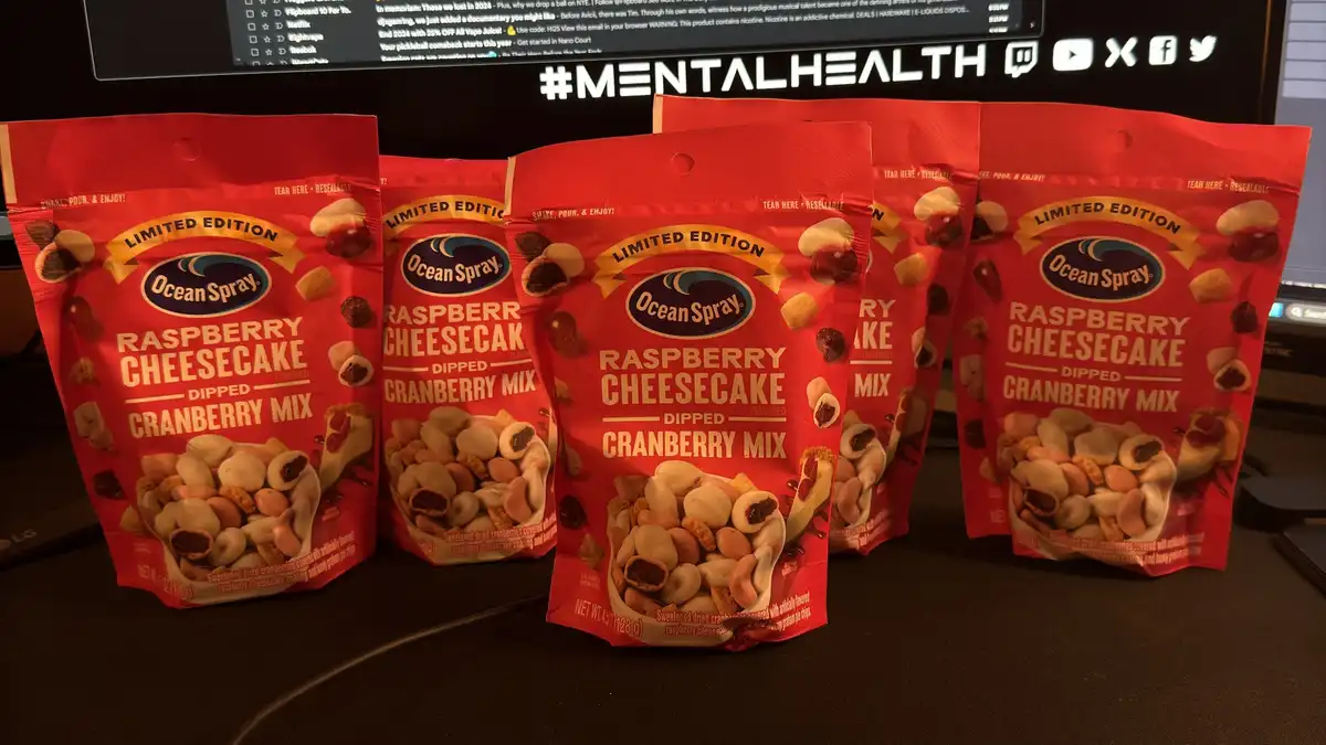 Five red bags of Ocean Spray's 'Limited Edition Raspberry Cheesecake Dipped Cranberry Mix' are arranged on a desk in front…