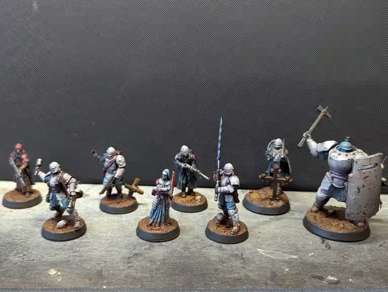 A row of eight painted miniature fantasy or sci-fi soldiers in armor, each on a circular base, arranged in a line against a…