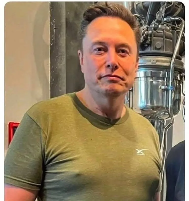 A man with short dark hair and a neutral expression wears a green t-shirt with a small white logo on the chest. Behind him…