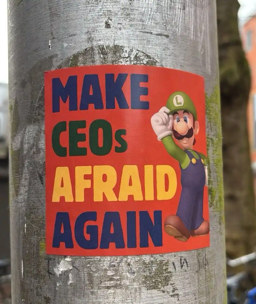 A red sticker on a weathered metal pole features the character Luigi from the Mario franchise, who is pointing at the…