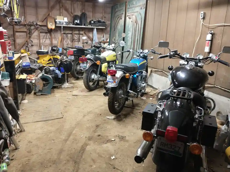 A cluttered garage filled with multiple motorcycles of various makes and colors, including a prominent black bike in the…