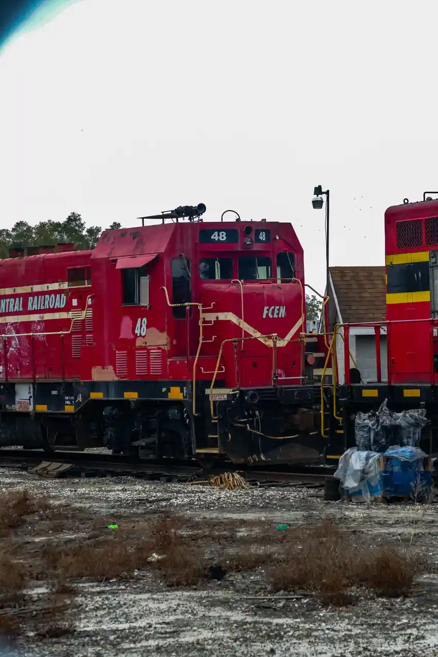 A red, weathered railroad locomotive, numbered 48 and marked 'FCEN' and 'CENTRAL RAILROAD', sits idle on tracks next to a…