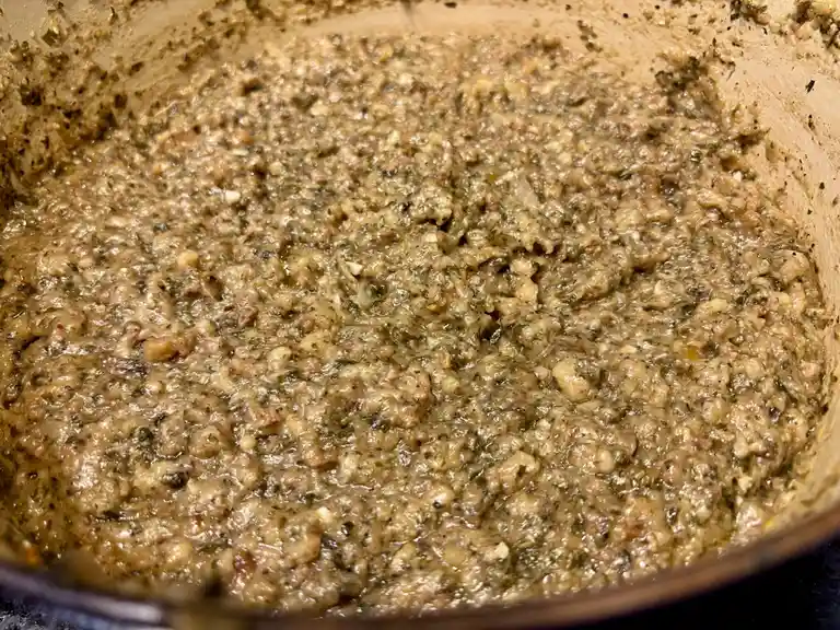 A close-up photo shows a thick, textured mixture of ground meat, herbs, and spices simmering in a pot. The overlaid text…