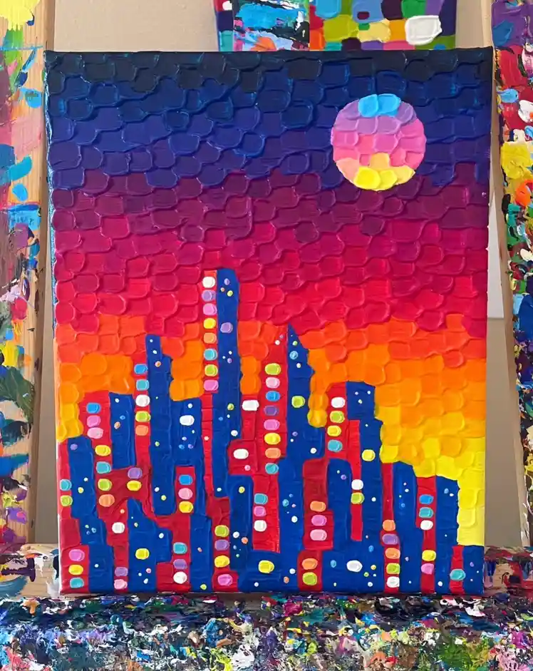 A thickly textured, colorful painting of a city skyline at sunset or sunrise, with blue buildings dotted with multicolored…