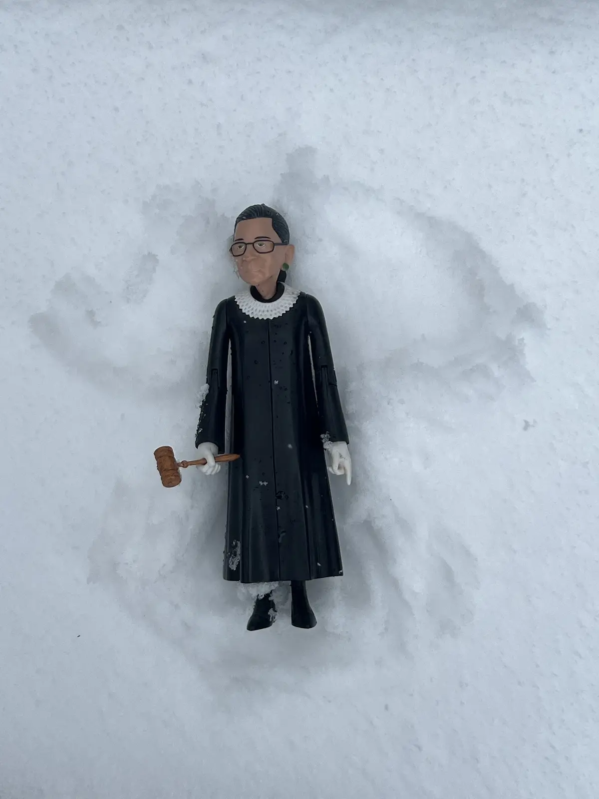 A plastic figurine of Ruth Bader Ginsburg, dressed in her black judicial robe with white collar and holding a gavel, is…