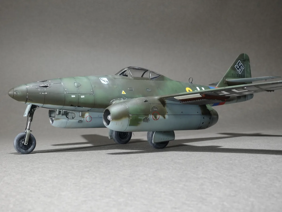 a detailed scale model of a german world war ii jet fighter, the me 262, is shown on a plain gray surface. The aircraft has…
