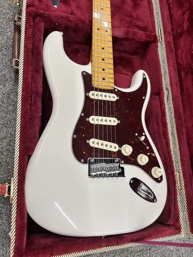 A white electric guitar with a tortoiseshell pickguard rests in a plush, burgundy-lined case. The overlaid text reads 'i…