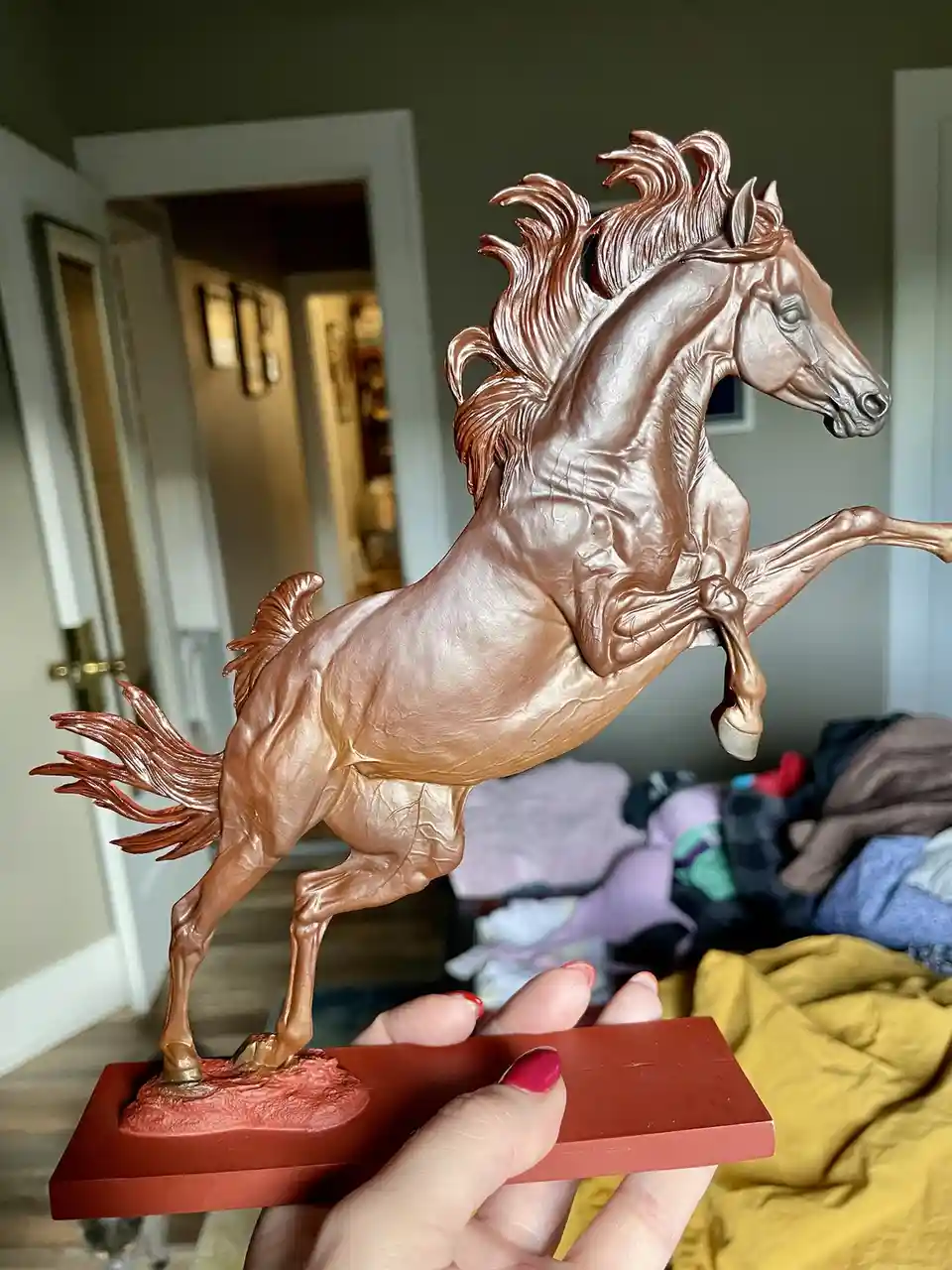 A person holds a detailed, bronze-colored horse statue in a dynamic rearing pose, mounted on a red base. The statue is being…