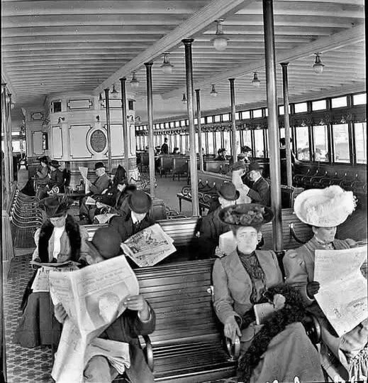 A vintage black-and-white photo shows several women in early 20th-century attire, including hats and long coats, seated on…
