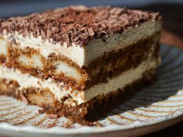 a close-up photo of a layered tiramisu dessert on a patterned plate, topped with chocolate shavings. The text overlaid on…