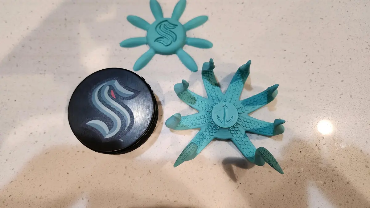 Three teal-colored, starfish-shaped objects with Seahawks logos sit on a speckled countertop next to a black hockey puck…