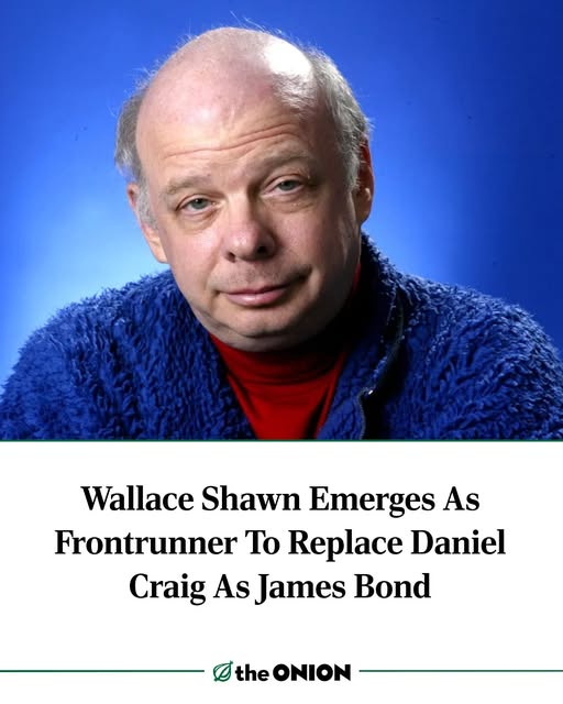 A headshot of actor Wallace Shawn, who has a balding head and is wearing a blue fuzzy jacket over a red turtleneck, against…