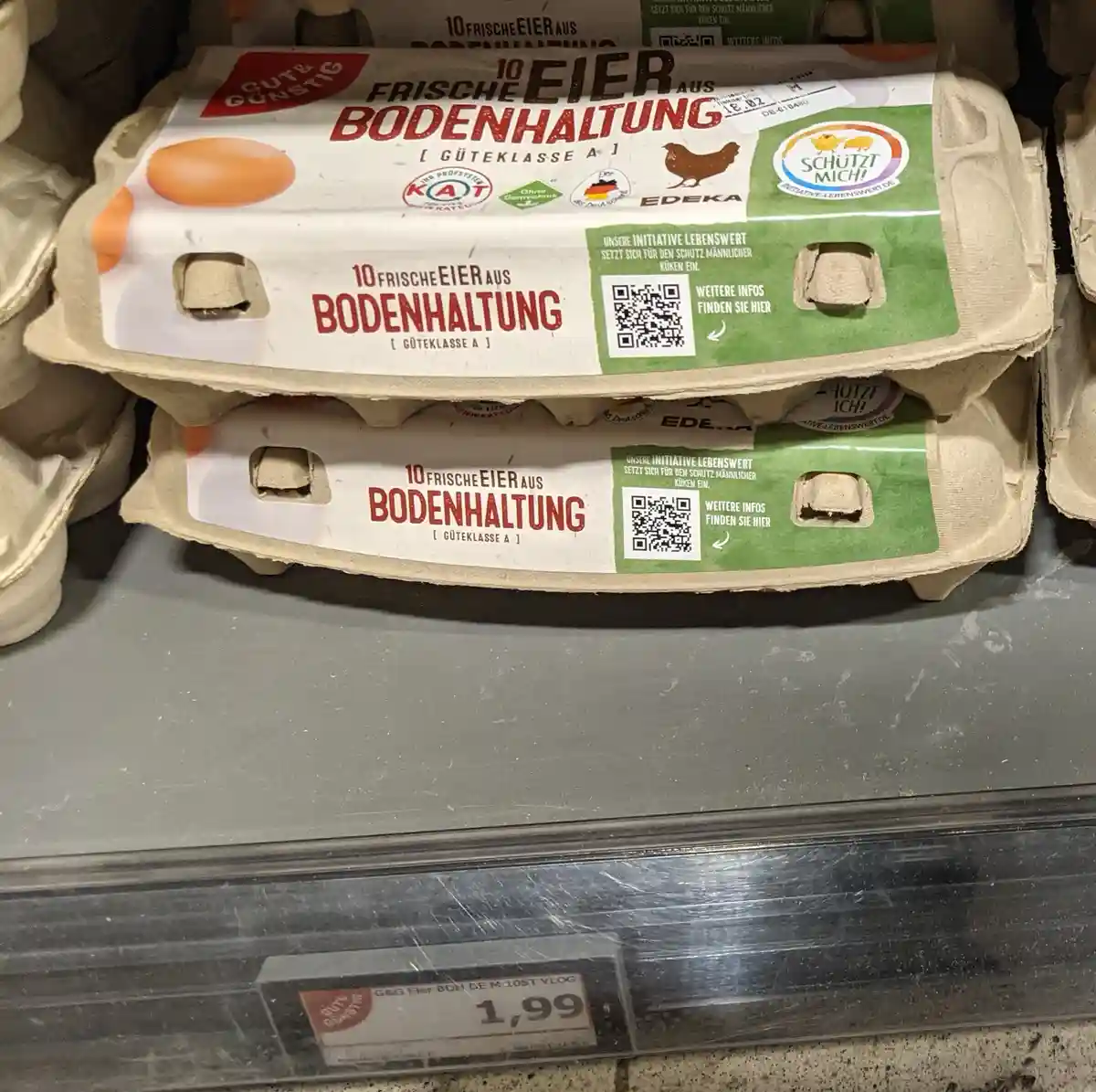 Two stacked cartons of EDEKA brand eggs are on a supermarket shelf, labeled '10 FRISCHE EIER AUS BODENHALTUNG [ GÜTEKLASSE A…