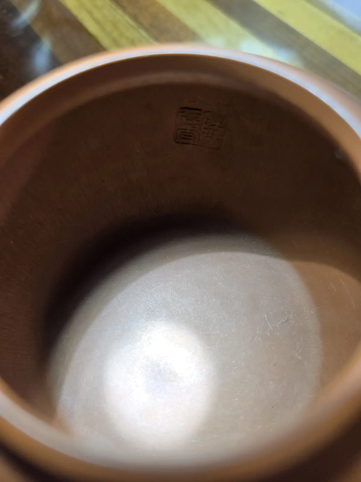 A close-up photo shows the inside of a brown ceramic bowl, with a small embossed maker's mark visible near the rim. The bowl…