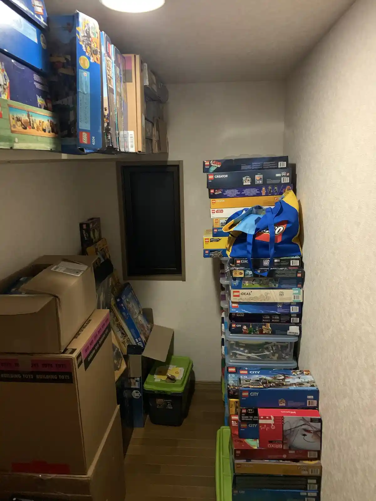 A narrow room is completely filled with stacks of Lego sets in their original boxes, piled high on shelves, on the floor…