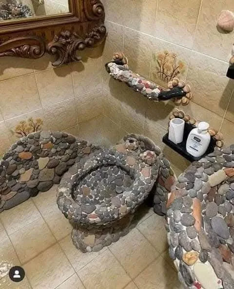 a bathroom features a toilet and matching sink entirely constructed from smooth, multicolored river stones, with a…