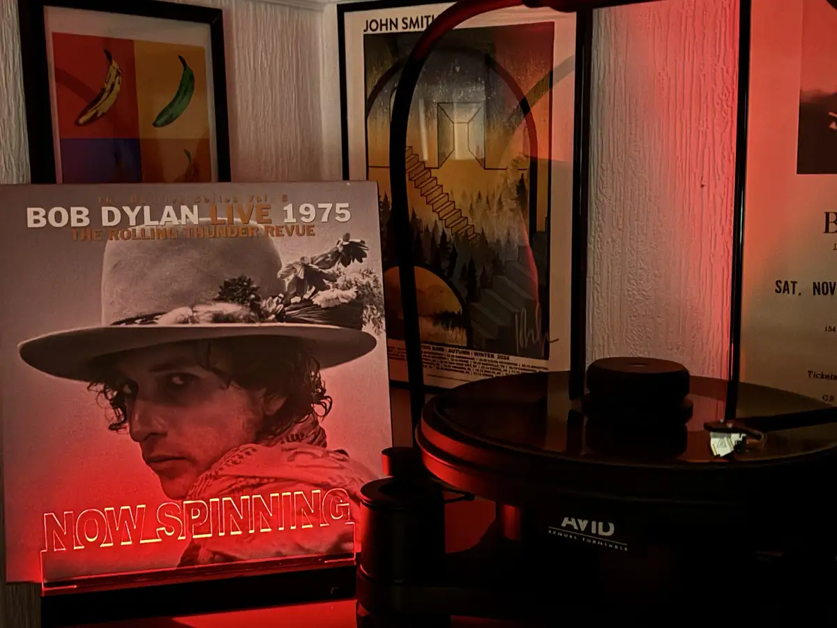 A vinyl record player sits next to a framed album cover for Bob Dylan's 'Live 1975 The Rolling Thunder Revue'. The album…